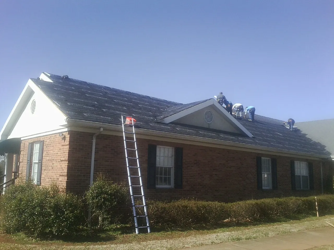 Crew tearing shingles off a brick ranch roof with a ladder set — Metal Roof Repair work by our crew in Knightstown