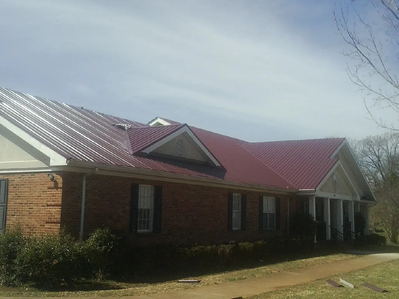 Red metal roof with gabled entries on a long brick building, from a Hail Damage Roof Repair job in Knightstown