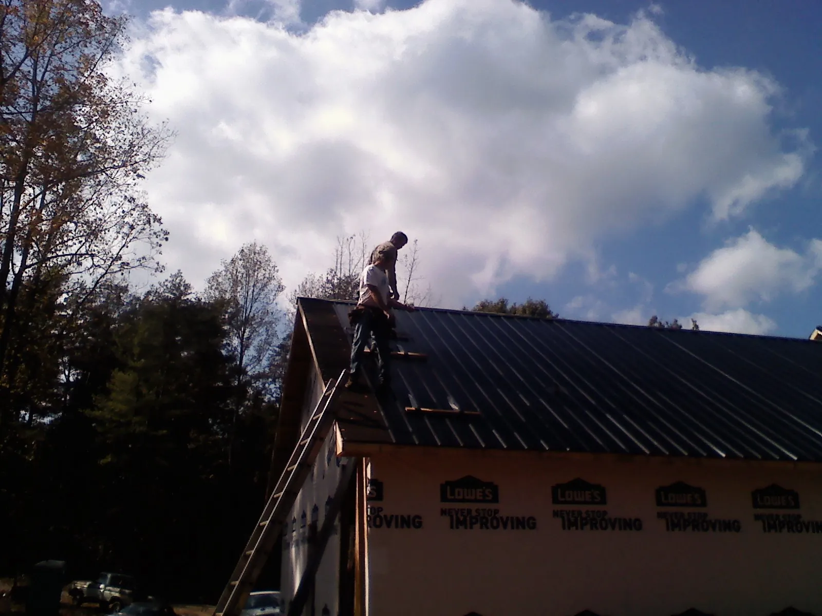 Roofer fastening dark metal panels high against a cloudy sky, from a Roof Inspection job in Knightstown