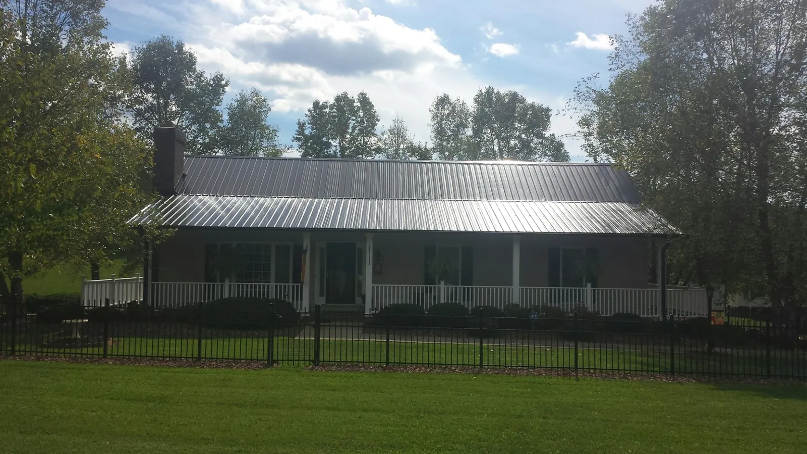 Gray metal roof on a brick ranch with a full width front porch — Gutter Guard Installation work by our crew in Knightstown