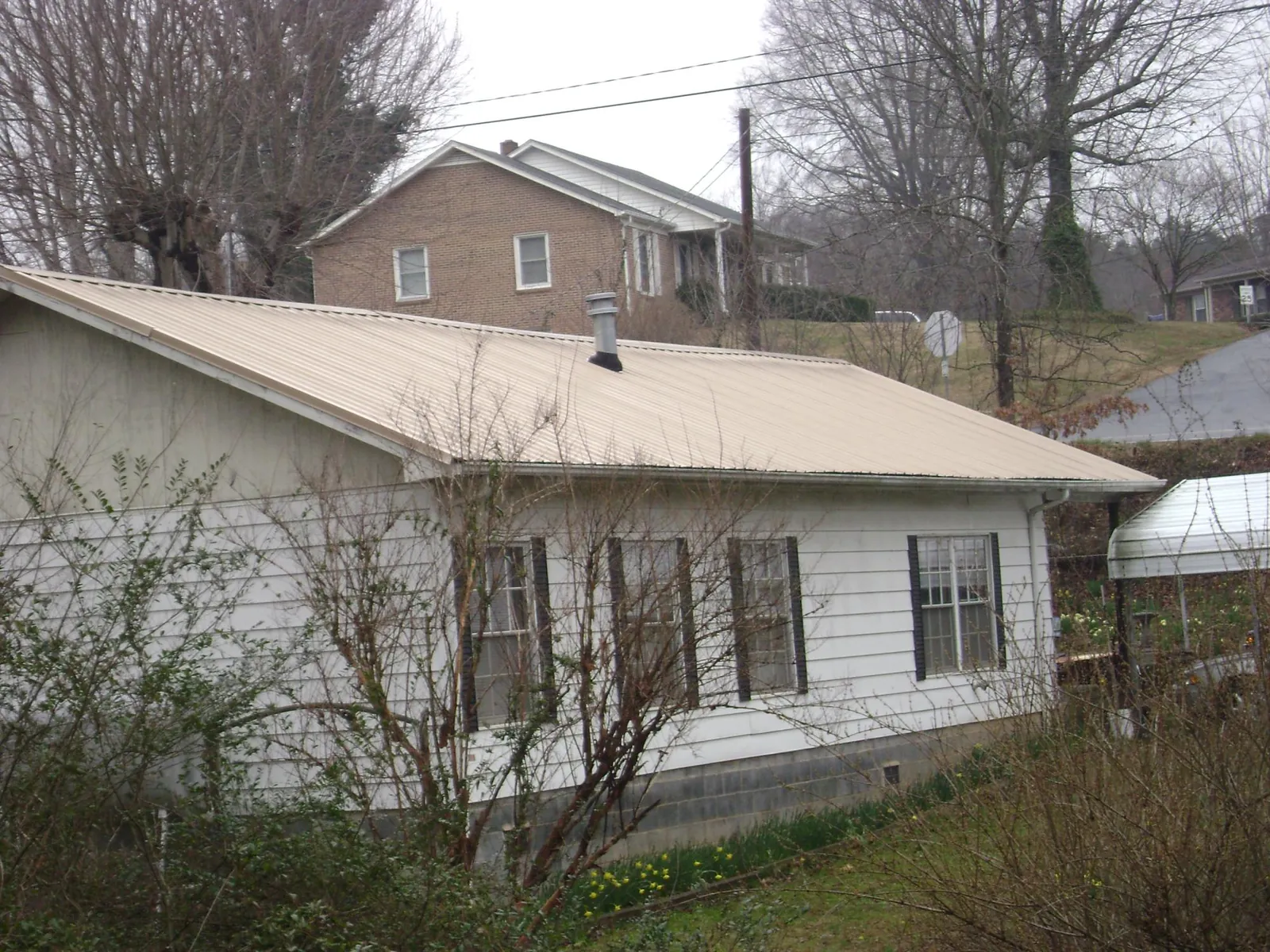 Tan metal roof on a white sided house set into a hillside — Commercial Roofing by Roofing Brothers in Knightstown