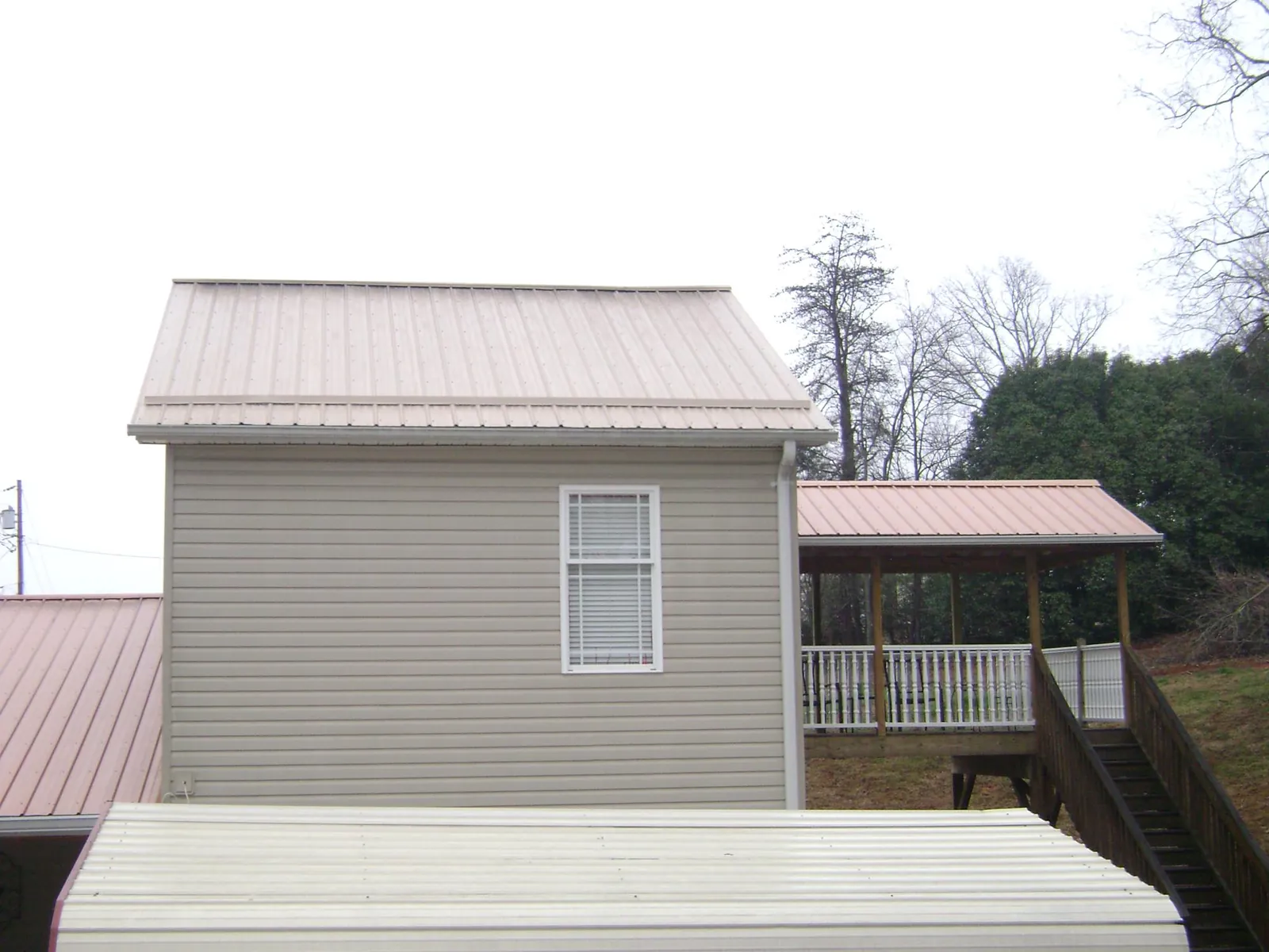 Tan metal roofs on a two story addition and attached porch, from a Roof Replacement job in Knightstown